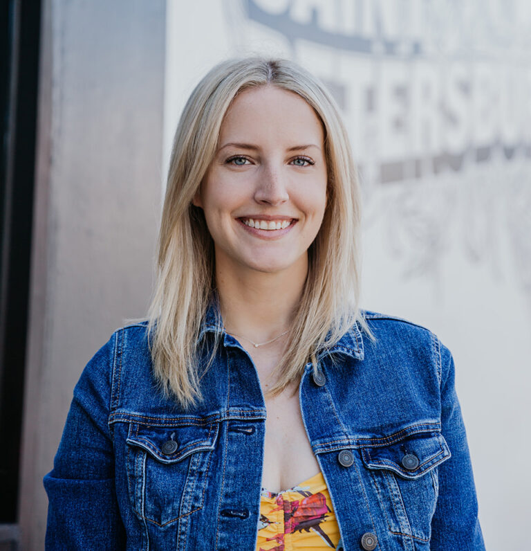 young blonde wearing a yellow and pink dress and a denim jacket against a mural