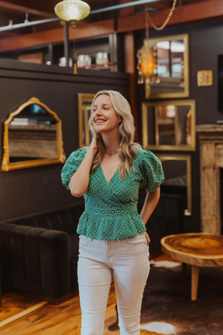 young blonde woman in a green blouse and white pants walking in a coffee shop